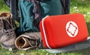 a red first aid kit on grass next to hiking gear