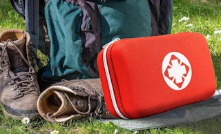 a red first aid kit on grass next to hiking gear