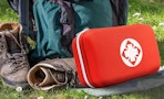a red first aid kit on grass next to hiking gear