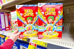 hand touching a box of lucky charms cereal on a shelf
