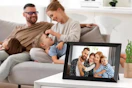 a digital photo frame on a table with a family on the couch in the background