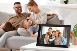 a digital photo frame on a table with a family on the couch in the background