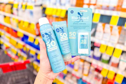 person holding 3 blue lizard sunscreens in front of shelves