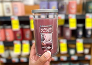 hand holding one Yankee Candle in front of Yankee candle display