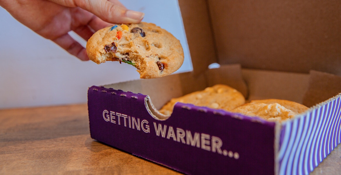 someone eating a cookie from Insomnia Cookies near a box of more cookies