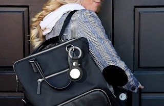 A person standing at a door with an airtag hanging from their bag
