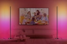 In a living room, a TV set is flanked by two smart RGBICW floor lamps, which are set to red, magenta, and yellow.