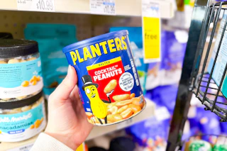 person holding a jar of planters peanuts in front of the shelf