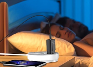 a phone plugged into an outlet on a nightstand next to a bed