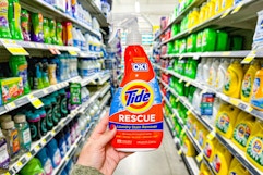 a hand holding a bottle of stain remover in a store's aisle 
