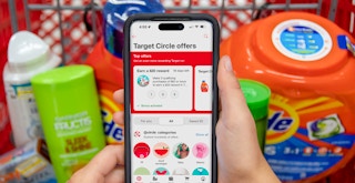 Someone holding a cell phone displaying the target circle app in front of a cart of groceries in Target