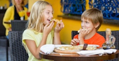 Two kids eating pizza together at a restaurant