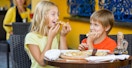 Two kids eating pizza together at a restaurant