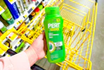 hand holdling a bottle of pert plus shampoo over yellow shopping cart