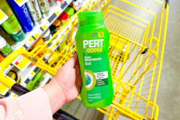 hand holdling a bottle of pert plus shampoo over yellow shopping cart