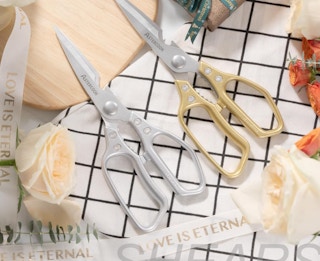 a silver and gold pair of shears on a grid table with flowers and ribbon