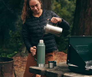 A woman pouring water into a Stanley water bottle.