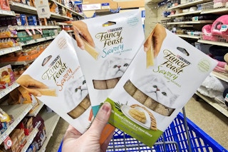hand holding 3 packs of fancy feast puree cat treats in an aisle