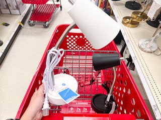 hand holding a white Room Essentials task table lamp in front of a Target cart holding a black Room Essentials task table lamo