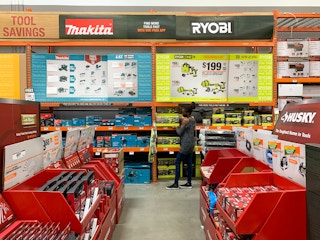 A person walking through the tool section at Home Depot with a clear view of Makita, Ryobi, and Husky brand signs.