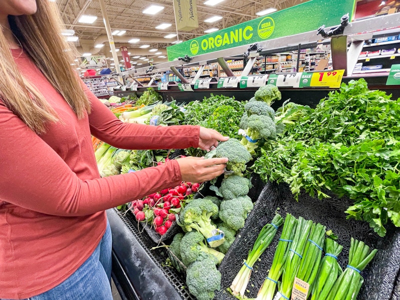 A person pulling a bundle of broccoli from a produce display in a grocery store.