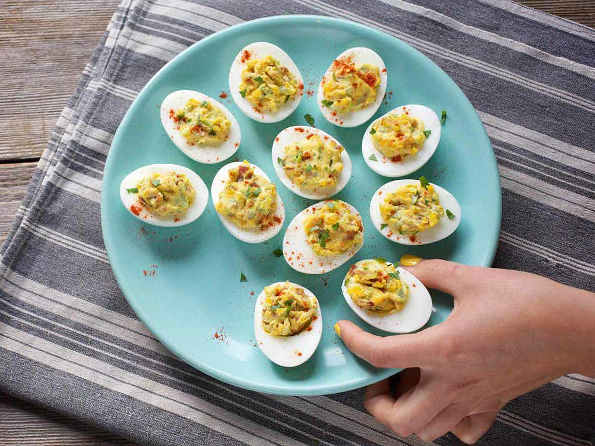 persons hand reaching for a deviled egg from a plate