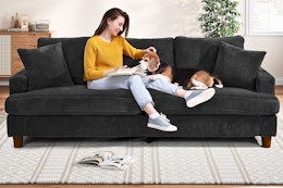 A black 87-inch corduroy sofa with woman and dog sitting on it in a home setting