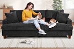 A black 87-inch corduroy sofa with woman and dog sitting on it in a home setting