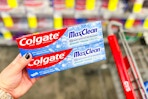 person holding 2 colgate toothpastes by a cart