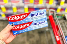 person holding 2 colgate toothpastes by a cart