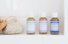 Three soap bottles and a sponge on a shelf in the shower