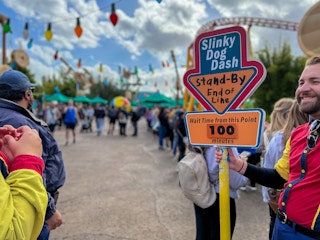 A Disney employee holding a sign for the Slinky Dog Dash ride, indicating that the wait time from that point is 100 minutes.