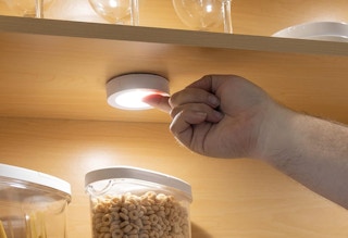 a hand turning on a tap light in a cabinet
