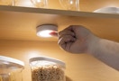 a hand turning on a tap light in a cabinet