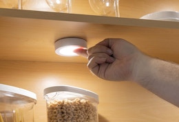 a hand turning on a tap light in a cabinet