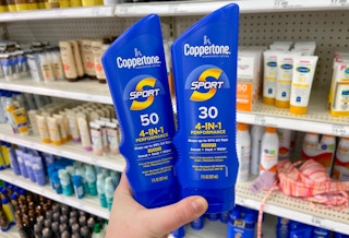 hand holding two bottles of coppertone sunscreen lotion in front of a shelf