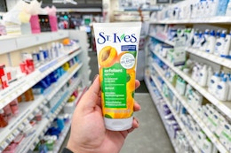 person holding a st ives face scrub in an aisle
