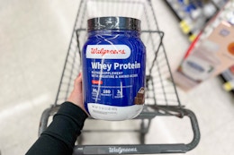 hand holding walgreens brand whey protein powder over shopping cart