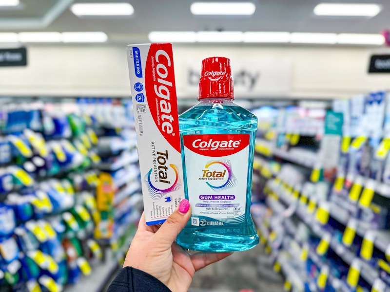 person holding colgate toothpaste and mouthwash in an aisle