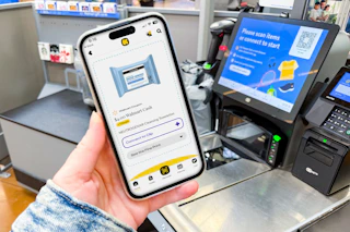 hand holding a smartphone that displays a kcl 1-clip coupon next to a self-checkout machine