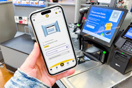 hand holding a smartphone that displays a kcl 1-clip coupon next to a self-checkout machine