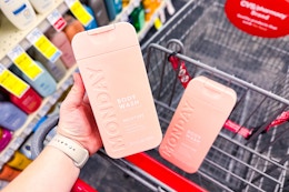 person placing a bottle of monday body wash in a cart with another bottle in it
