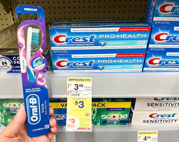 A person holding an oral-b toothbrush next to a shelf holding crest pro-health toothpaste