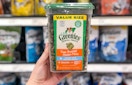 a hand holding a container of cat treats in a store aisle