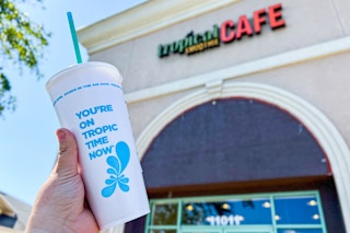 a peerson holding up a smoothie in front of a tropical smoothie cafe