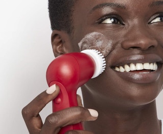 a woman using a red cleansing brush on her face