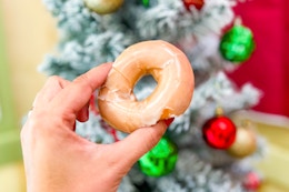 someone holding a Krispy Kreme donut in front of a Christmas tree