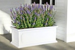 Lifestyle image of the allen + roth resin planter outside with purple flowers planted inside