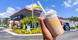a hand holding a oreo frappe from mcdonalds outside of the restaurant