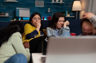 Friends sitting on a couch cringing at a scary movie playing on the laptop in front of them.